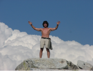 Mike standing on a rock with arms raised against clouds
